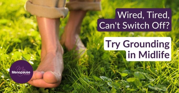 Midlife woman standing barefoot on grass, practicing grounding outdoors