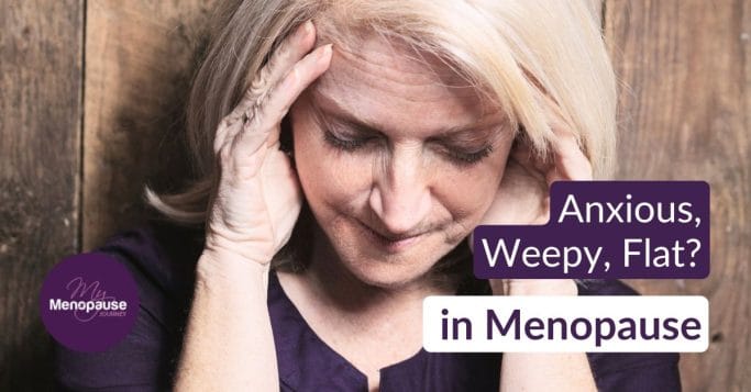 Midlife woman holding her head against a wooden wall, overwhelmed by low mood in menopause